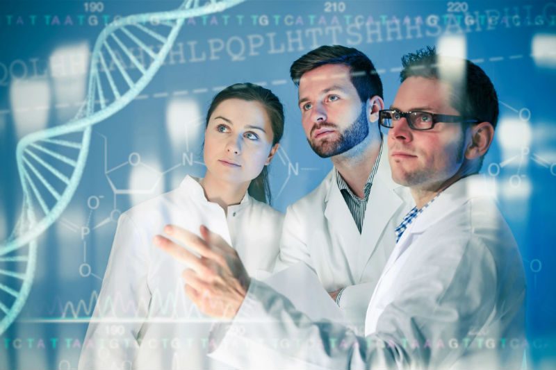 Three people in lab coats are looking at a screen.